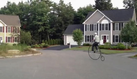 Input image: man on a penny-farthing bicycle in front of a suburban house
