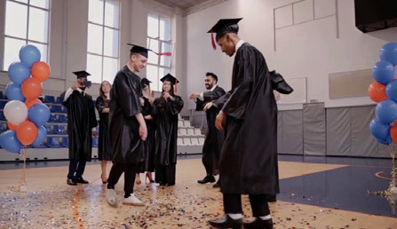 Input image: graduates in gowns and caps in a well-lit hall